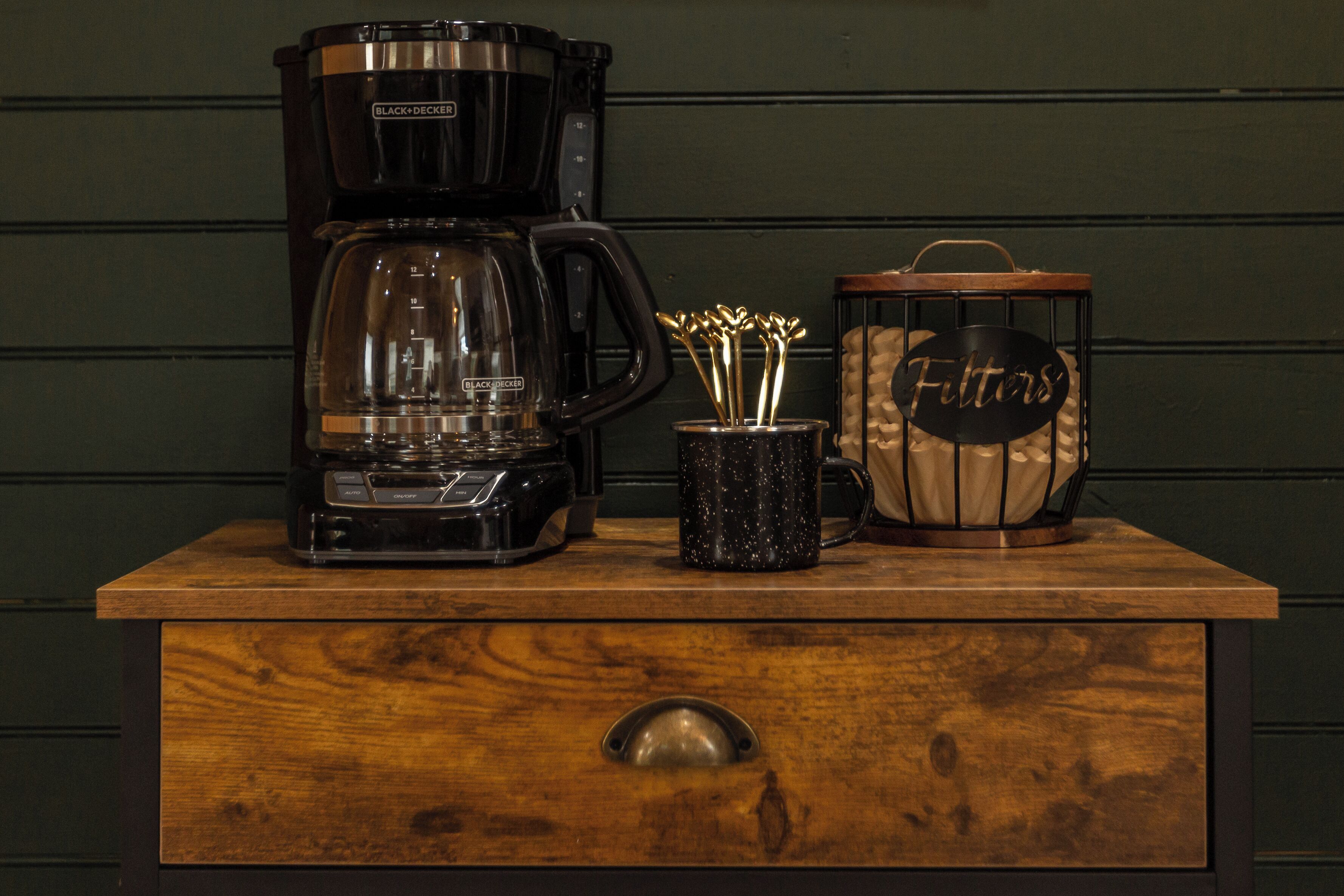 Una cafetera, una taza con asa y un recipiente con tapa sobre una superficie de madera.