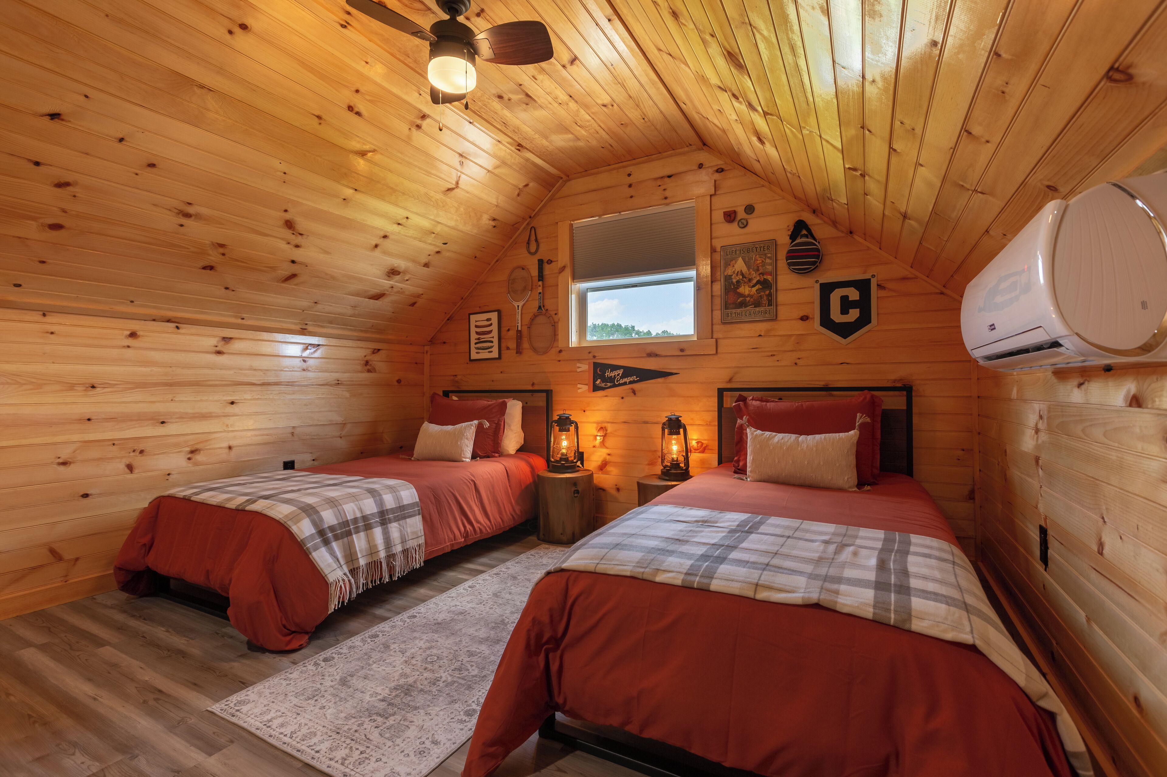 Ein gemütliches Schlafzimmer im Dachgeschoss mit zwei Betten, Holzwänden, einem Fenster und einem Deckenventilator.