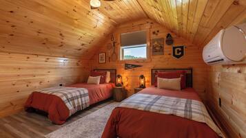 Ein gemütliches Schlafzimmer im Dachgeschoss mit zwei Betten, Holzwänden, einem Fenster und einem Deckenventilator.