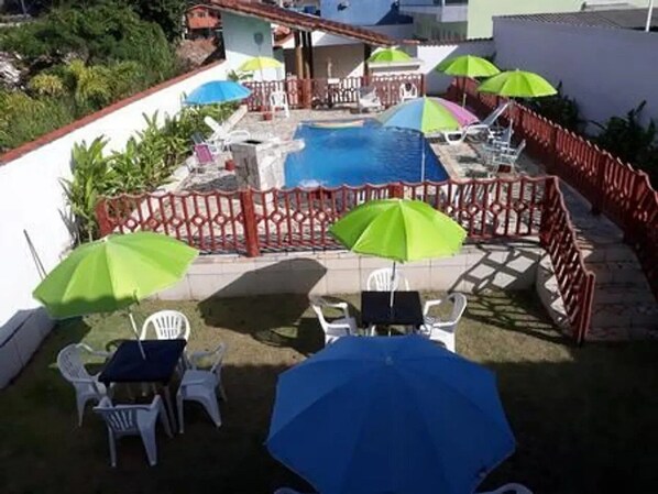 A pool area with a red fence, green umbrellas, and white chairs. - POUSADA TANI COM PISCINA em MARESIAS (São Sebastião)