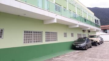 A multi-story building with a green and white facade, a glass balcony, and a parking area with two cars.