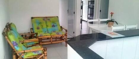 A room with a kitchen area, a dining table, and two chairs with floral upholstery.