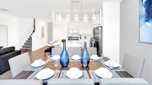A modern dining area with a wooden table set for six, blue vases, and a chandelier. - UpstaySleeps20ThemeRoomsPoolHotTubTheatr (Kissimmee)