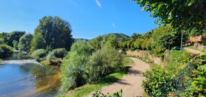 A river with a dirt path alongside it, surrounded by greenery and trees.