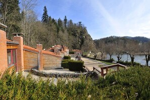 Une propriété située au bord du lac, avec un bâtiment en briques, des marches en pierre et une terrasse en bois offrant une vue sur l’eau.