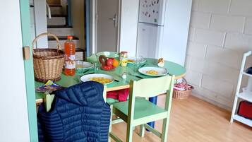 A small, cozy room with a dining table set for two, a green chair, a blue jacket hanging on the chair, and a wooden floor.
