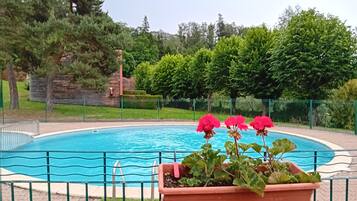 A swimming pool surrounded by a green fence, with a flower pot containing pink flowers in the foreground.