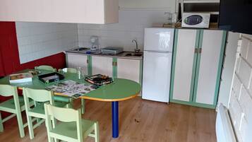 A compact kitchen with a dining table, chairs, a refrigerator, and a microwave.