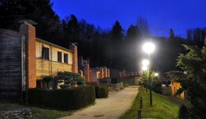 Un chemin menant à un bâtiment à la façade en briques et au revêtement en bois, entouré de verdure et éclairé par des lampadaires.