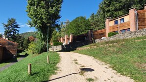 Un sentiero sterrato conduce a un edificio con muro in pietra e rivestimento in legno, immerso nel verde e alberi.