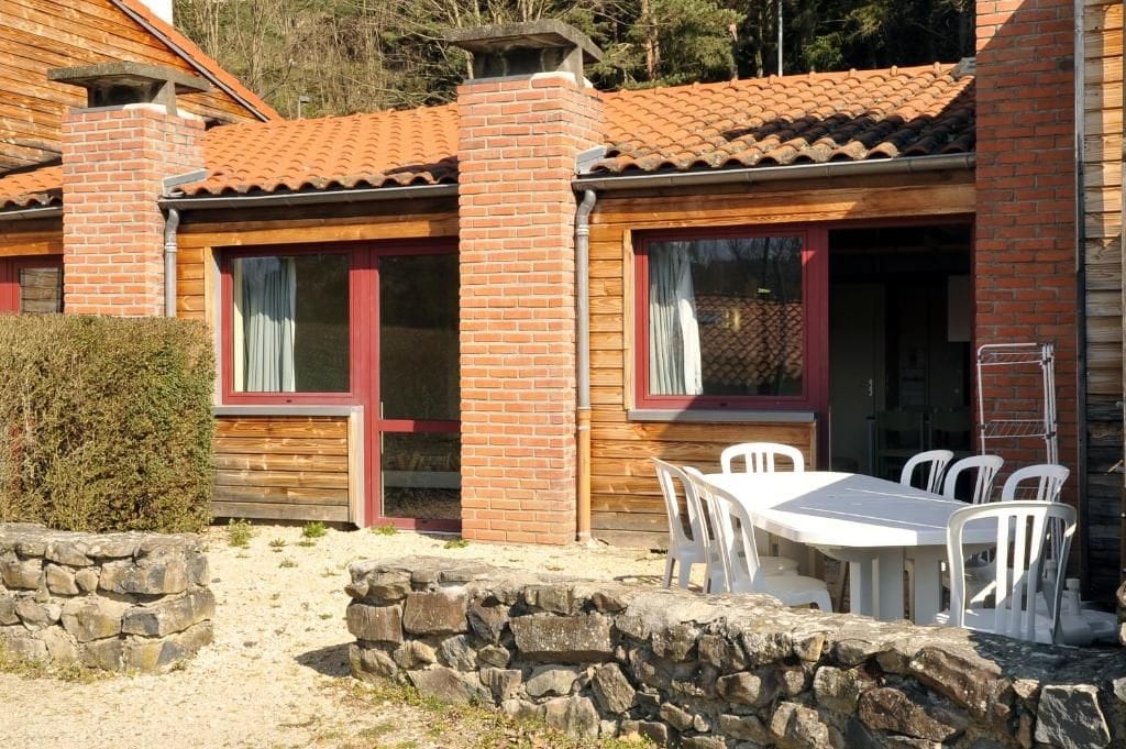 A wooden cabin with a tiled roof, a stone wall, and a white table with chairs outside.