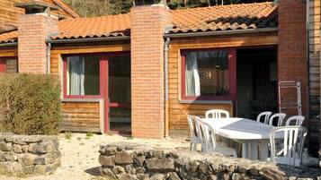 A wooden cabin with a tiled roof, a stone wall, and a white table with chairs outside.