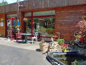 Un bâtiment en bois comprenant un espace d’accueil, des sièges à l’extérieur et un petit étang agrémenté de fleurs.