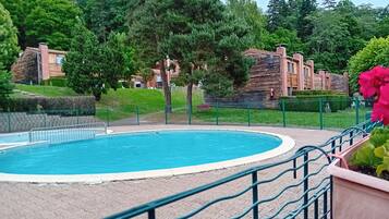 A swimming pool with a surrounding fence, greenery, and buildings in the background.