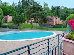 A swimming pool with a surrounding fence, greenery, and buildings in the background. - Olydea Vorey sur Arzon (Vorey)