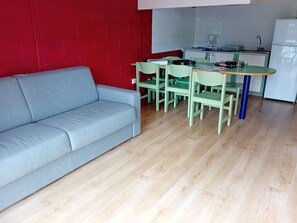 A compact living space with a grey sofa, a dining table with chairs, and a kitchenette area.