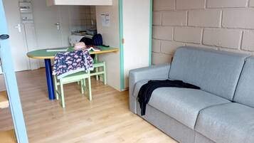 A room with a grey sofa, a green table with a book and a hat, and a wooden floor.