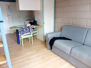 A room with a grey sofa, a green table with a book and a hat, and a wooden floor. - Olydea Vorey sur Arzon (Vorey)
