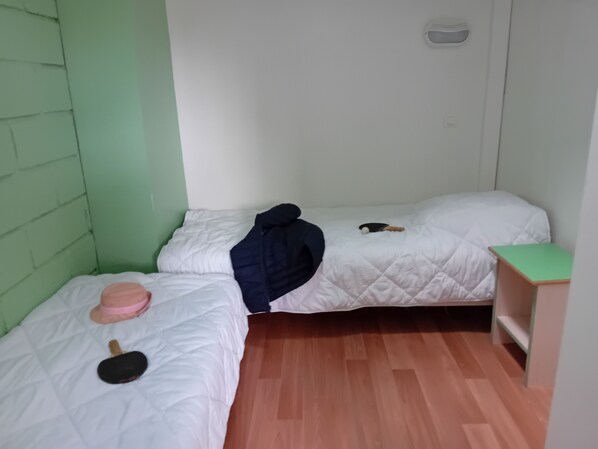 Una habitación pequeña y funcional con dos camas individuales, suelo de madera y pared verde.