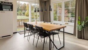 Une cuisine moderne dotée d’un four encastré, d’un coin repas avec une table en bois et des chaises noires, et de grandes fenêtres offrant une vue sur l’extérieur.