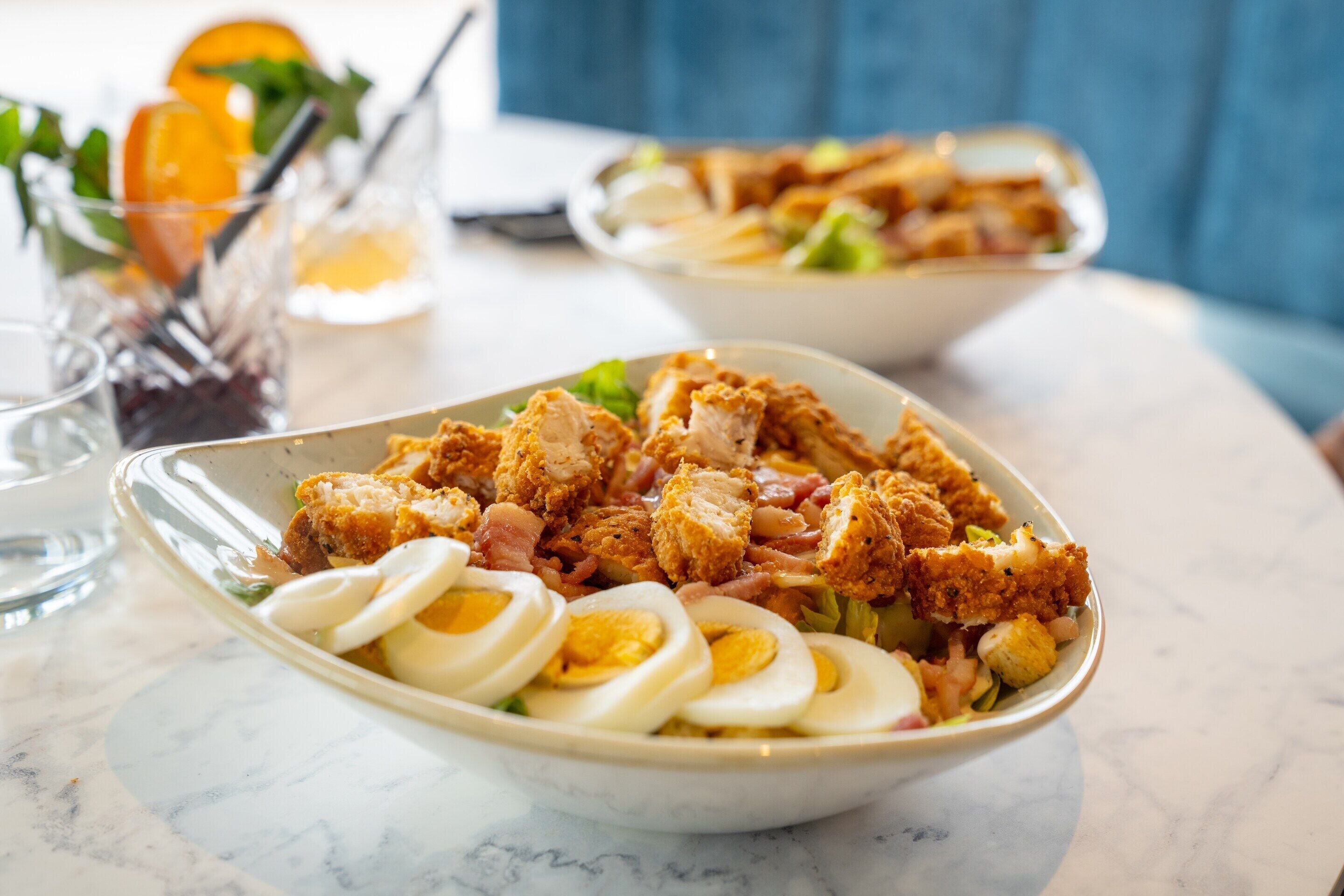 Un bol rempli de nourriture, comprenant du poulet frit, des œufs et des légumes, posé sur une table en marbre.