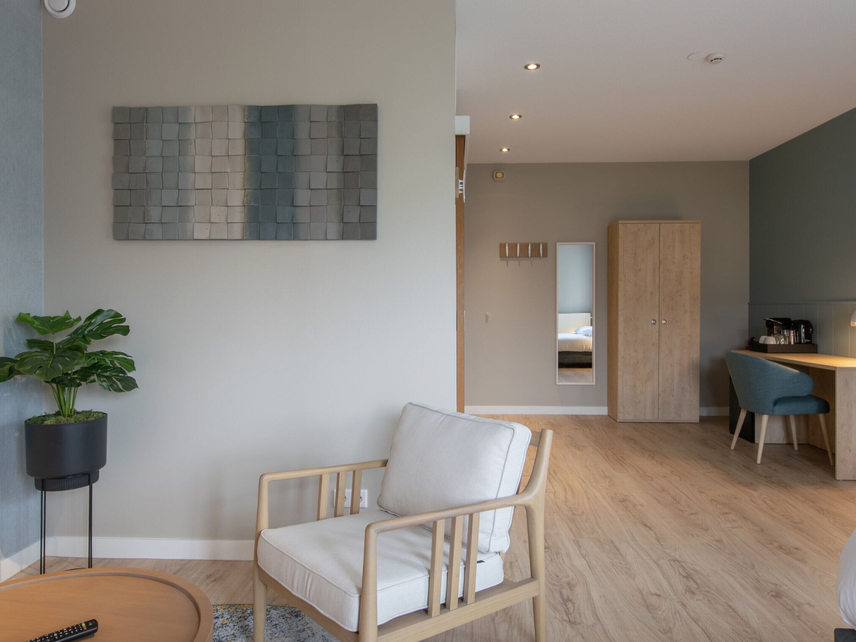 A modern living room with a wooden chair, a potted plant, and a wall-mounted artwork.