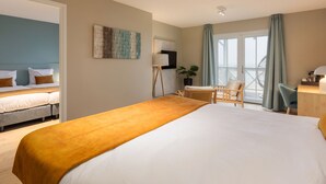 Une chambre d’hôtel avec un grand lit, un bureau, une chaise, une plante en pot et une vue sur l’extérieur par une fenêtre.