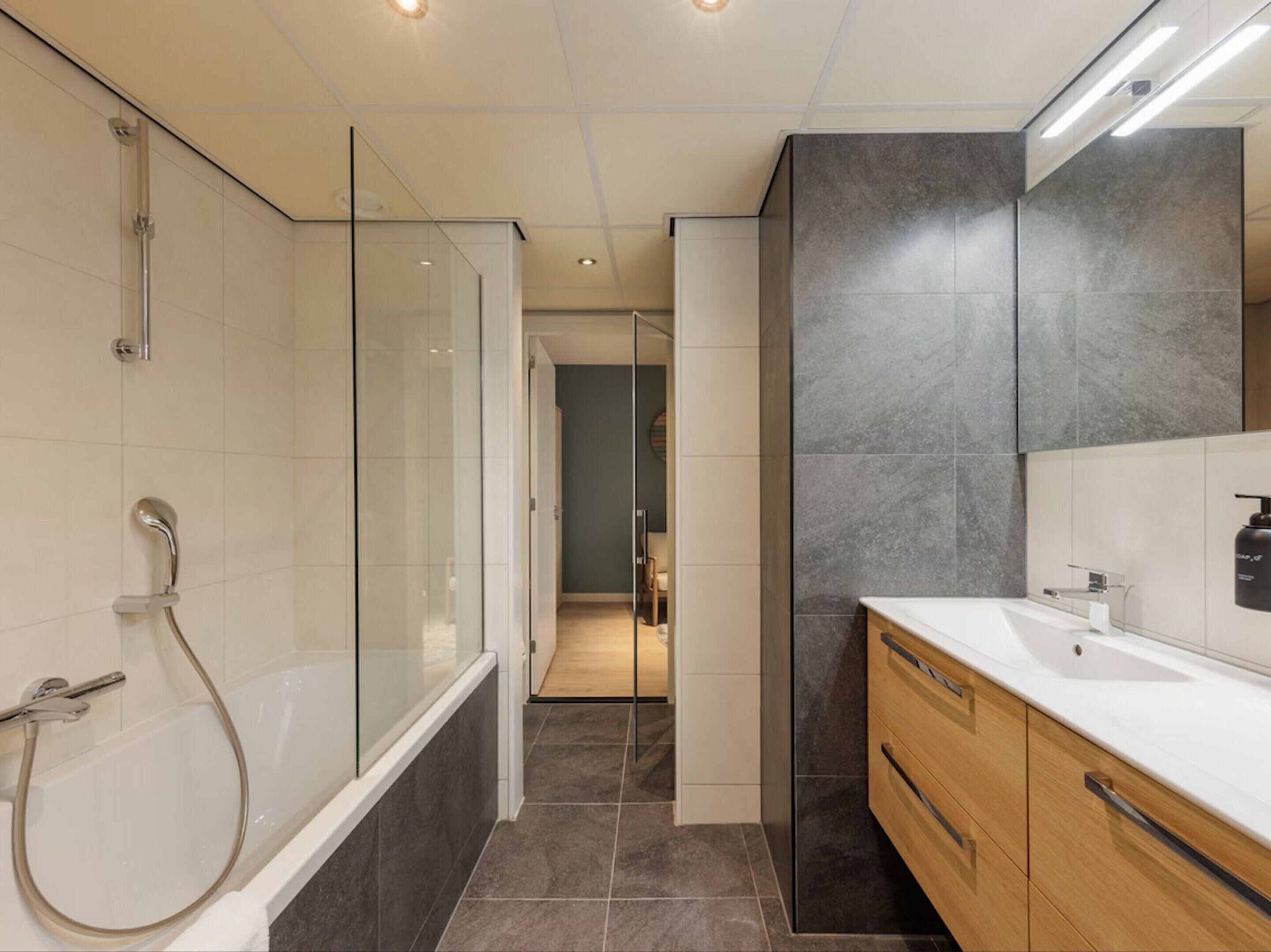 Un baño moderno con cabina de ducha de vidrio, tocador de madera y un espejo grande.