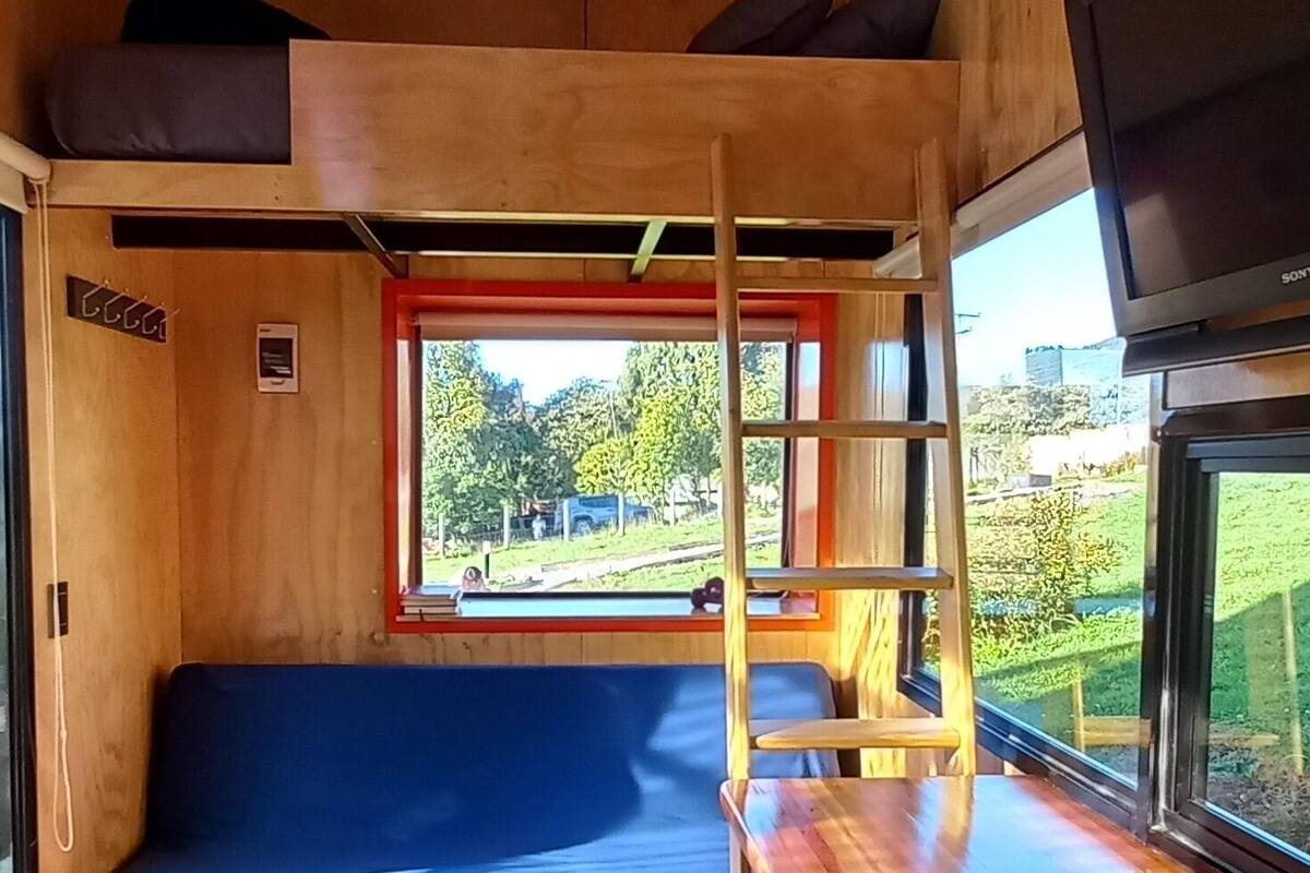 Un intérieur compact en bois, avec un lit superposé, un canapé bleu, une table en bois et un téléviseur.
