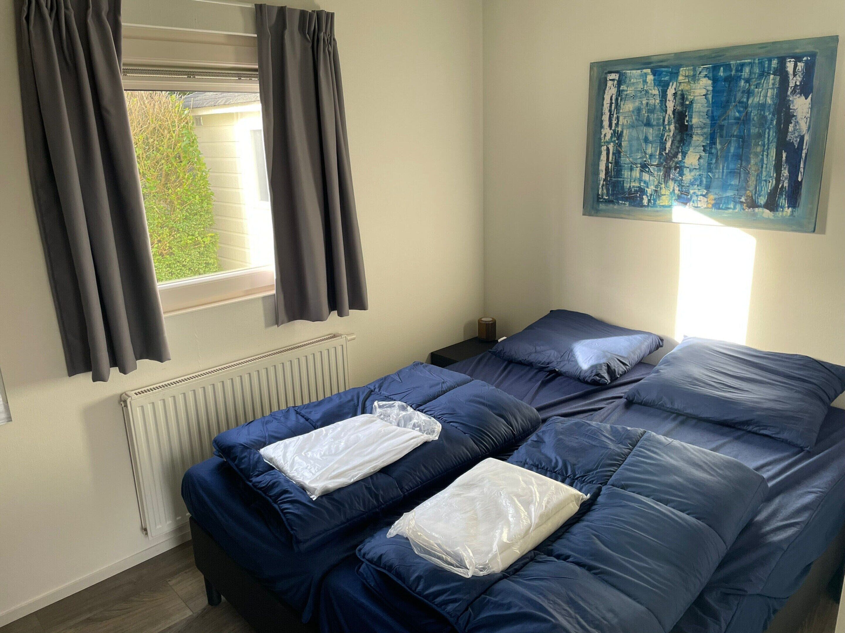 A room with a bed, a radiator, a window with curtains, and a painting on the wall.