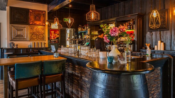 A bar area with a wooden bar counter, multiple seating options, and decorative lighting fixtures.