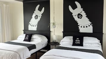 A hotel room with two beds, each with a black headboard featuring a white llama design and a pillow with the text "NO drama llama".