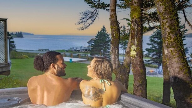 Una pareja en un jacuzzi con vistas al océano y árboles.