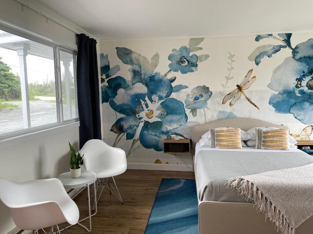 A bedroom with a bed, a nightstand, a chair, a plant, and a window with curtains.