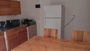 Eine kleine Küche mit Holzausstattung, einem weißen Kühlschrank, einer Mikrowelle und einem Holzessttisch.