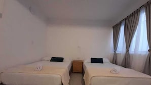 Ein Zimmer mit zwei Betten, einem Nachttisch und einem Fenster mit Vorhängen.