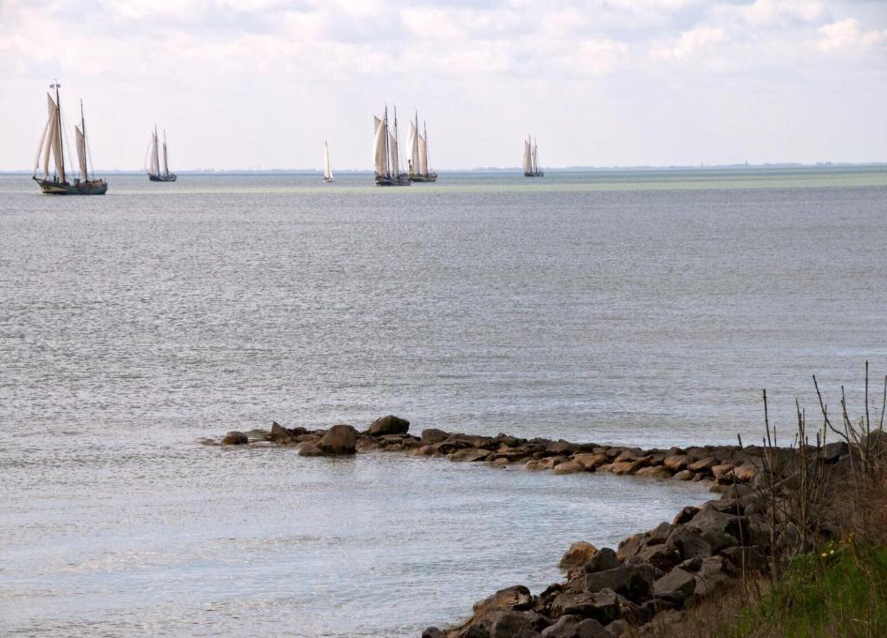 Escena costera con veleros en el agua y un litoral rocoso.