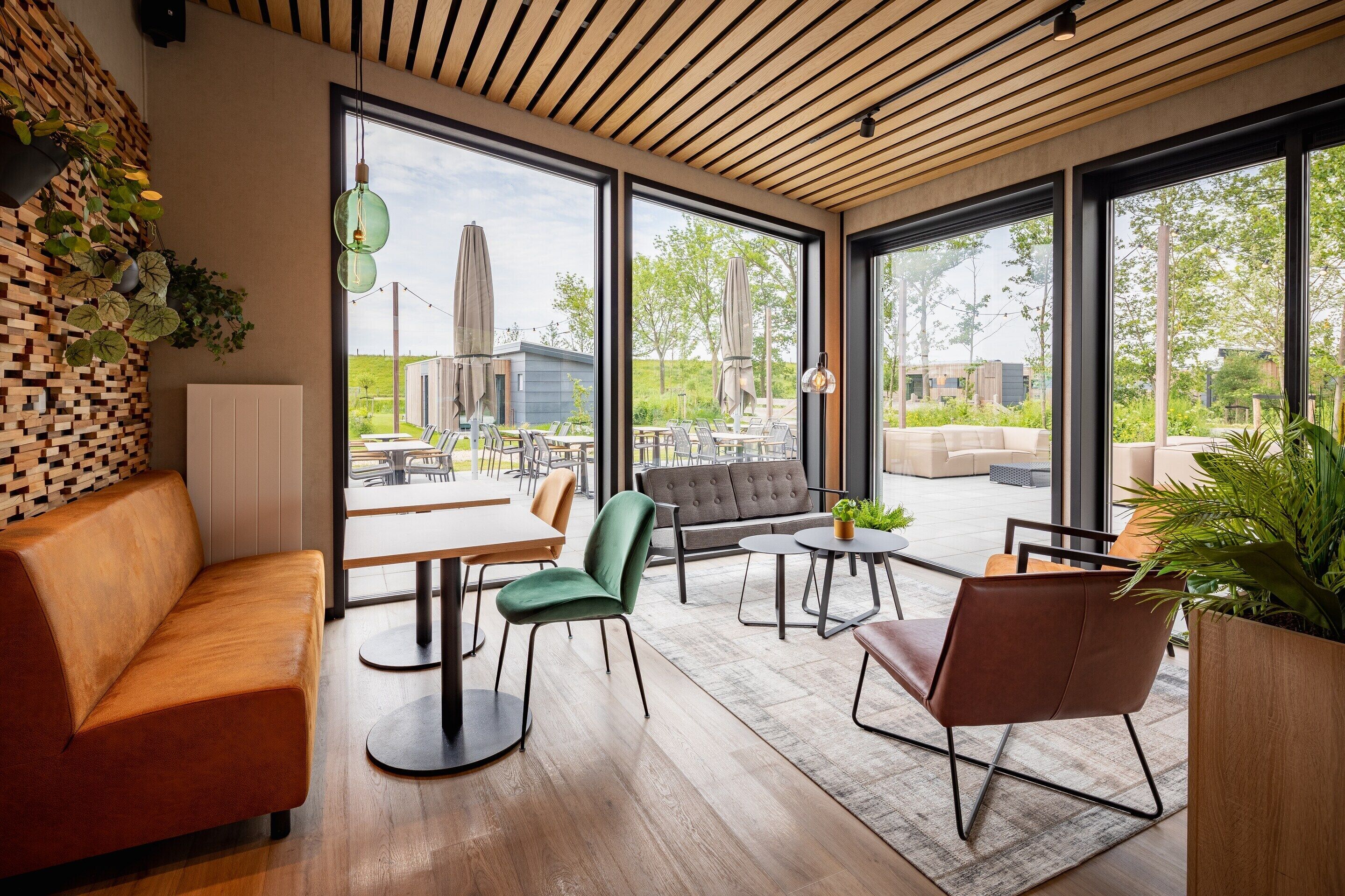 A modern interior with a wooden ceiling, large windows, and a mix of seating arrangements including a sofa, chairs, and tables.