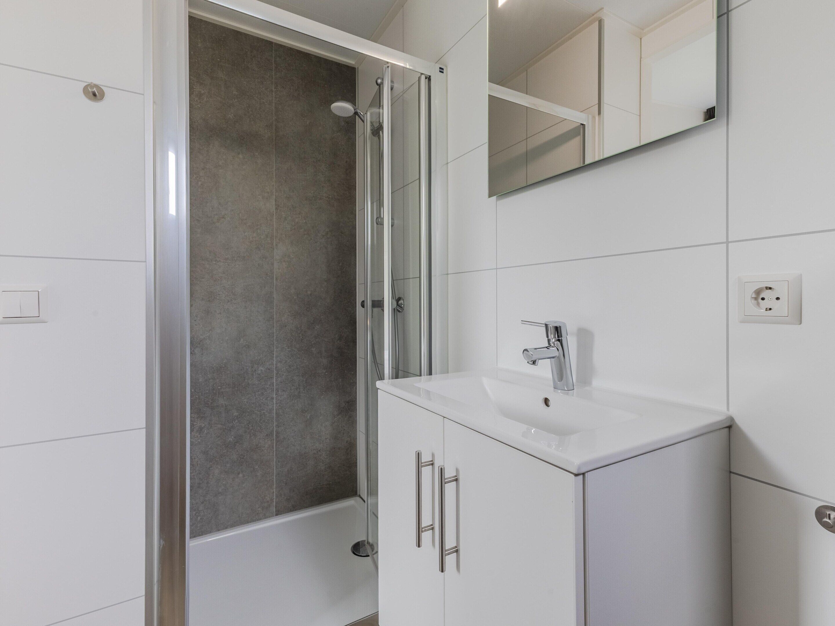 Ein modernes Badezimmer mit einer gläsernen Dusche, einem weißen Waschbecken und einem Spiegel darüber.
