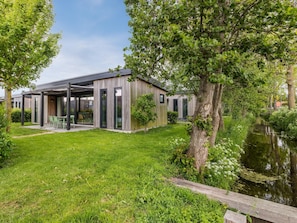 Una casa moderna amb un porxo cobert, un estany i vegetació exuberant.