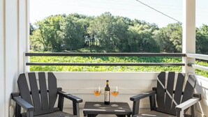 A covered outdoor seating area with two Adirondack chairs and a small table, featuring a bottle of wine and two glasses.