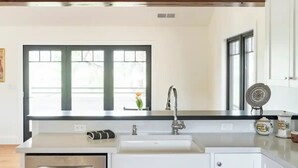 A modern kitchen with white cabinetry, a stainless steel dishwasher, and a large window above the sink.