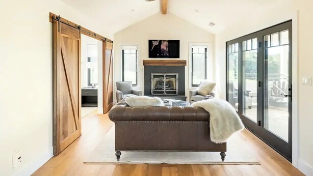 A spacious living room with a fireplace, a large window, and a sliding door leading to another room.