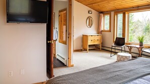 Un dormitorio con cama, cómoda, silla, mesita, espejo y televisor montado en la pared.