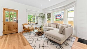 A spacious living room with a large beige sectional sofa, a wooden chair, a glass coffee table, and a patterned rug. - * The Bungalow at Hyde Park * (Boise)