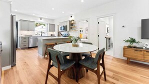 A modern kitchen with a central island, a dining area with a round table and chairs, and a living space with a TV and a plant. - * The Bungalow at Hyde Park * (Boise)