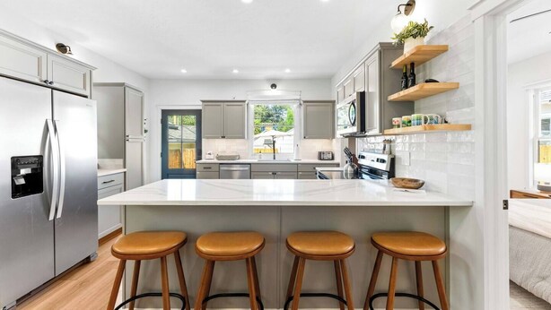 A modern kitchen with a central island, bar stools, stainless steel appliances, and wooden shelves. - * The Bungalow at Hyde Park * (Boise)