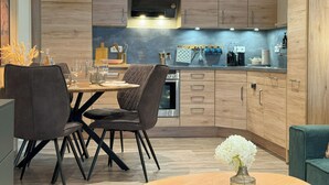 Une cuisine moderne avec des meubles en bois, un îlot central doté de chaises, un luminaire suspendu et un four encastré.