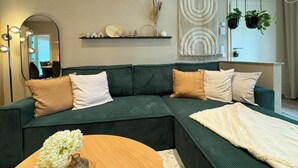 Un salon moderne avec un canapé d’angle vert, une table basse ronde en bois et un élément décoratif mural.
