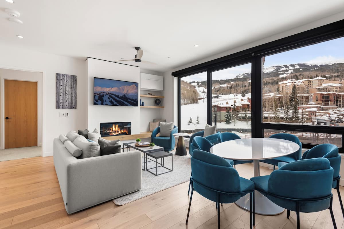 Una sala de estar moderna con chimenea, un televisor grande y vistas a un paisaje montañoso nevado.